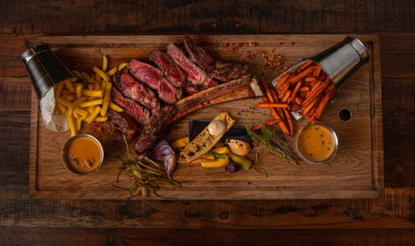 Sliced Tomahawk steak with sides on a wooden board at MEAT30, steakhouse in Brussels